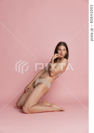 Portrait of young beautiful tanned woman in lingerie posing isolated over pink studio background. Natural beauty concept. Portrait of young beautiful tanned woman in lingerie posing isolated over pink studio background. Natural beauty concept. 80643005