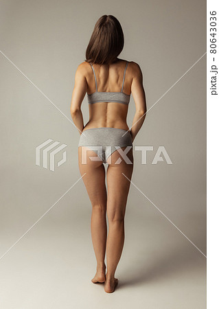 Portrait of young beautiful slim woman in lingerie posing isolated over gray studio background. Natural beauty concept. Back view Portrait of young beautiful slim woman in lingerie posing isolated over gray studio background. Natural beauty concept. Back view 80643036