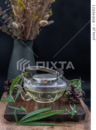 Cannabis herbal tea in teapot and Stem with green marijuana leaves on wooden background. 80646921