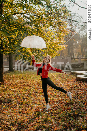 Hello fall, autumn season, fall mood, positive emotions. Teenager girl jumping with transparent umbrella and enjoying life in autumn sunny park Hello fall, autumn season, fall mood, positive emotions. Teenager girl jumping with transparent umbrella and enjoying life in autumn sunny park 80647619