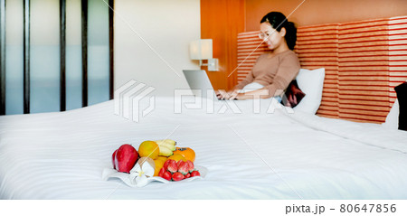 Fruits in tray in front of tourists used laptop on the bed in the luxury hotel room Fruits in tray in front of tourists used laptop on the bed in the luxury hotel room 80647856