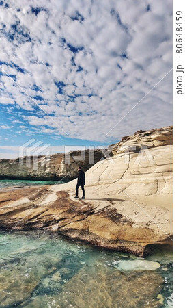 Grotto White stones. Grotto "White stones" is a very picturesque place located near the city of Limassol, next to the beach of Alamanos. A man in black is standing on a cliff looking at clear water 80648459