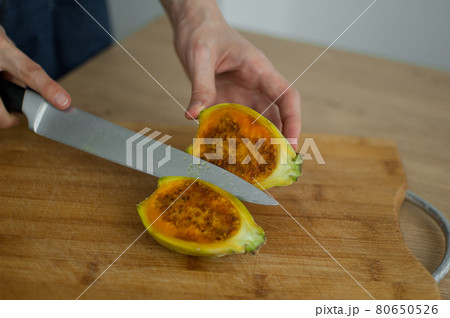 Female hands is cutting a fresh ripe cactus pear on a cut wooden board. Exotic fruits, healthy eating concept. Female hands is cutting a fresh ripe cactus pear on a cut wooden board. Exotic fruits, healthy eating concept. 80650526