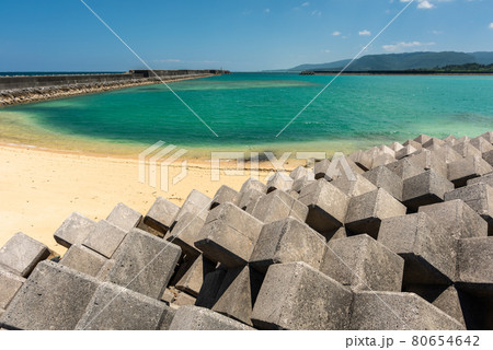 Amazing tropical town beach, crystal clear dark emerald green sea, smooth sands, long pier, tide blocks, blue sky, mountains. Iriomote Island. Amazing tropical town beach, crystal clear dark emerald green sea, smooth sands, long pier, tide blocks, blue sky, mountains. Iriomote Island. 80654642