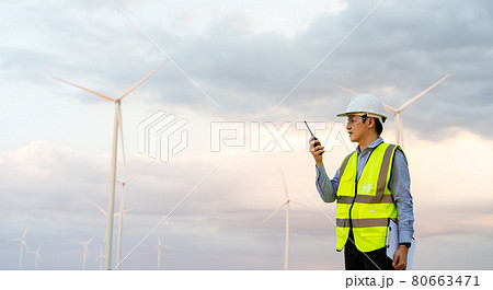 male engineer using walkie talkie to checking system against wind turbine farm 80663471