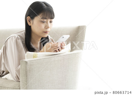 窓際のソファーで寝そべってスマホを操作する女性 80663714