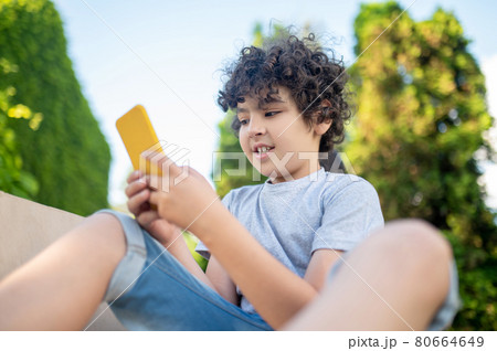 Curly boy looking into smartphone in nature Curly boy looking into smartphone in nature 80664649