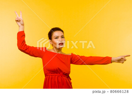Beautiful woman in red dress pointing finger on yellow background Beautiful woman in red dress pointing finger on yellow background 80666128