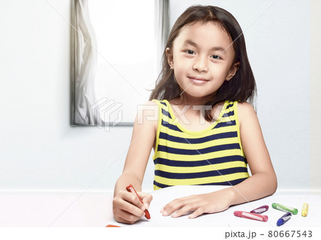 Asian little girl with a crayon drawing on the paper on the table Asian little girl with a crayon drawing on the paper on the table 80667543