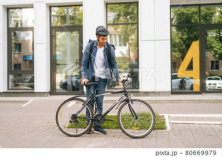 Cheerful courier male getting out of client apartment, sitting on bicycle and riding off to next delivery. Cheerful courier male getting out of client apartment, sitting on bicycle and riding off to next delivery. 80669979