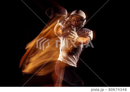 Portrait of young man, American football player training isolated on dark studio background with mixed neon light. Concept of sport, competition and beauty 80674348