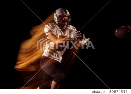 Portrait of young man, American football player training isolated on dark studio background with mixed neon light. Concept of sport, competition and beauty Portrait of young man, American football player training isolated on dark studio background with mixed neon light. Concept of sport, competition and beauty 80674355
