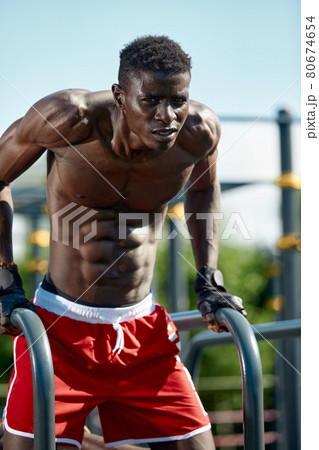 Black fitness man exercising dips, cross training of male model in urban environment. An African guy in his twenties is training on the street. 80674654