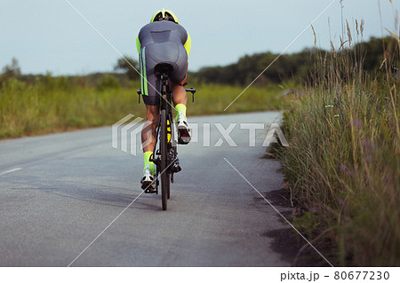 Young male triathlete riding a bicycle on the open road. Professional sportsman is engaged in triathlon on bright summer day Young male triathlete riding a bicycle on the open road. Professional sportsman is engaged in triathlon on bright summer day 80677230