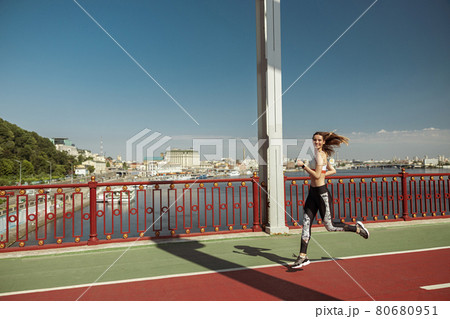 Sportswoman with flying hair runs along footbridge on sunny day Sportswoman with flying hair runs along footbridge on sunny day 80680951