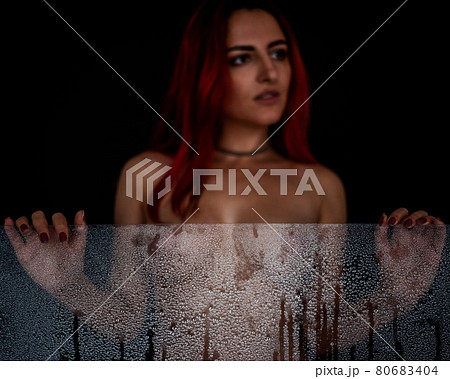 Beautiful naked woman holding a misted glass in her hands in drops of water. Focus on the glass. Black background 80683404