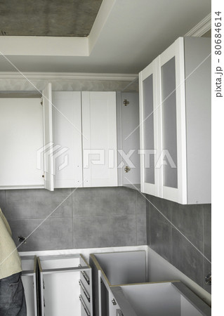 Custom kitchen cabinets installation with a white furniture facades mdf. Gray modular kitchen from chipboard material on a various stages of installation. A frame furniture fronts mdf profile. 80684614