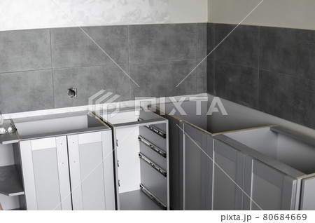 Lower custom kitchen cabinets installation with a furniture facades mdf. Gray modular kitchen from chipboard material on a various stages of installation. A frame furniture fronts mdf profile. Lower custom kitchen cabinets installation with a furniture facades mdf. Gray modular kitchen from chipboard material on a various stages of installation. A frame furniture fronts mdf profile. 80684669