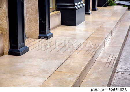 doorstep of beige glossy marble floor covering on the porch in the entrance to the store with black wooden columns on the facade of the building close-up of architectural design, nobody. 80684828