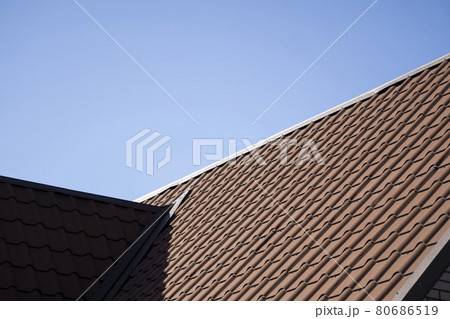 Brown corrugated metal profile roof installed on a modern house. The roof of corrugated sheet. Roofing of metal profile wavy shape. Modern roof made of metal. Metal roofing. Brown corrugated metal profile roof installed on a modern house. The roof of corrugated sheet. Roofing of metal profile wavy shape. Modern roof made of metal. Metal roofing. 80686519