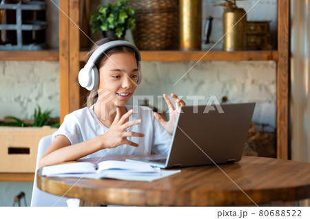 Photo of a schoolgirl during an online lesson. She does her homework online and answers the teacher's questions. 80688522