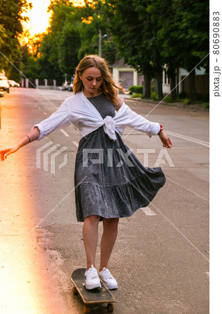Millennial Woman in dress riding a skateboard on street. Skater girl on a longboard. Cool female skateboarder at sunset. Carefree female skater 20s enjoying freedom youth lifestyle Hobby Millennial Woman in dress riding a skateboard on street. Skater girl on a longboard. Cool female skateboarder at sunset. Carefree female skater 20s enjoying freedom youth lifestyle Hobby 80690883