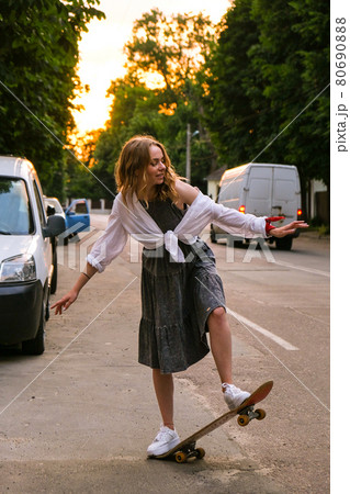 Millennial Woman in dress riding a skateboard on street. Skater girl on a longboard. Cool female skateboarder at sunset. Carefree female skater 20s enjoying freedom youth lifestyle Hobby Millennial Woman in dress riding a skateboard on street. Skater girl on a longboard. Cool female skateboarder at sunset. Carefree female skater 20s enjoying freedom youth lifestyle Hobby 80690888