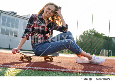 Young millennial woman hippie sitting on skateboard. Summer Skate Sessions. Woman cruising on a longboard in a park. Carefree female skater 20s enjoying freedom youth lifestyle 80690891