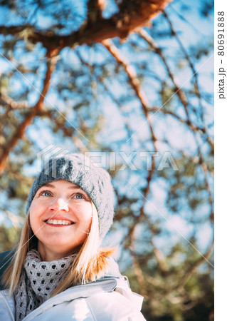 Young Caucasian Lady Woman Dressed In White Jacket And Grey-blue, Gray Hat Posing Near Pine Tree. Close Up Portrait. beautiful young woman smiling Young Caucasian Lady Woman Dressed In White Jacket And Grey-blue, Gray Hat Posing Near Pine Tree. Close Up Portrait. beautiful young woman smiling 80691888