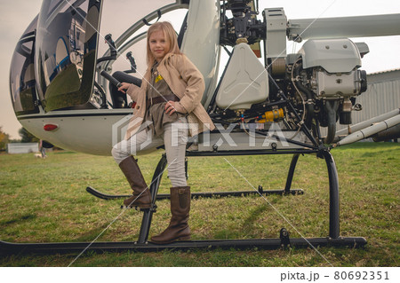 Blond preteen girl posing near open helicopter on flying field Blond preteen girl posing near open helicopter on flying field 80692351