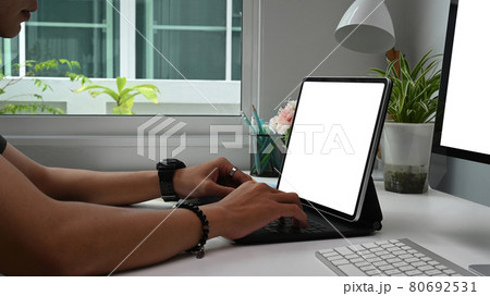 Cropped shot of concentrated young man freelancer is typing on computer tablet with blank screen while sitting at working place. 80692531