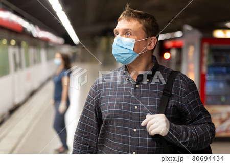 Male in protective medical mask is traveling and waiting train on platform in the metro. 80694434