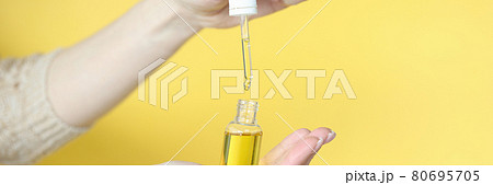 Female hands holding bottle of cosmetic oil on yellow background closeup 80695705