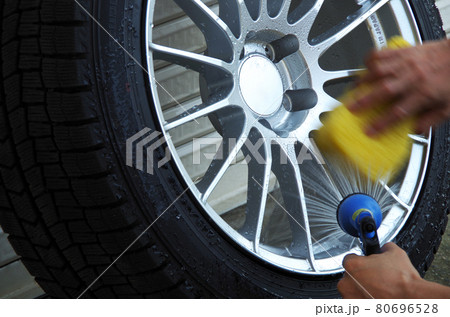 冬タイヤのホイールの表側を手作業で丁寧にシャワーとスポンジで水洗いしている光景 80696528
