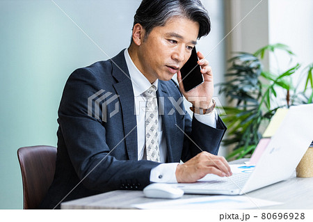パソコンの画面を見ながらスマホで通話しているビジネスマン 80696928