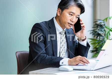 パソコンの画面を見ながらスマホで通話しているビジネスマン 80696929