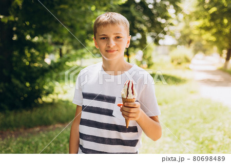 Teenager boy eating ice-cream cone on green nature background. Summer, junk food and people concept Teenager boy eating ice-cream cone on green nature background. Summer, junk food and people concept 80698489