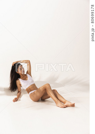Portrait of young beautiful tanned woman in white underwear lying on floor over white background. 80699178