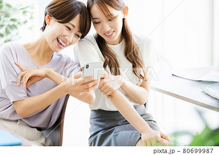 後ろの席の同僚とスマホを見ながら話をする2人のビジネスウーマン 後ろの席の同僚とスマホを見ながら話をする2人のビジネスウーマン 80699987