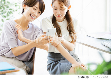 後ろの席の同僚とスマホを見ながら話をする2人のビジネスウーマン 後ろの席の同僚とスマホを見ながら話をする2人のビジネスウーマン 80699988