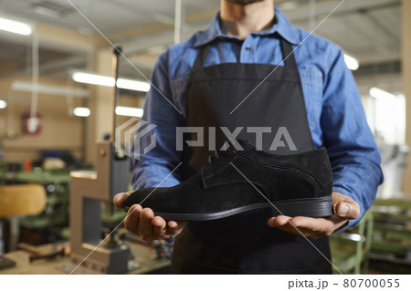 Footwear factory worker standing in the workshop and holding a new black suede boot 80700055