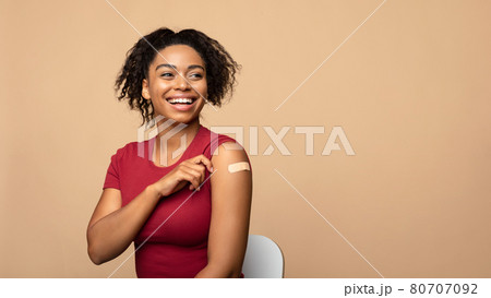 Cheerful vaccinated black woman showing arm with bandage after coronavirus vaccine injection on beige background 80707092