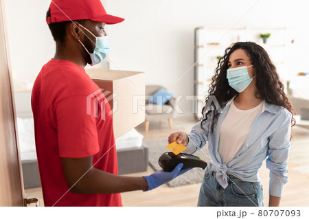 Black deliveryman holding nfc terminal lady paying with bankcard Black deliveryman holding nfc terminal lady paying with bankcard 80707093