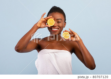 Excited african american lady with lemon halves in hands, posing wrapped in towel over blue background 80707120