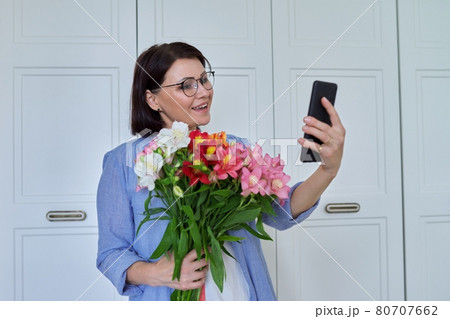 Happy middle-aged woman with large bouquet of flowers and smartphone Happy middle-aged woman with large bouquet of flowers and smartphone 80707662