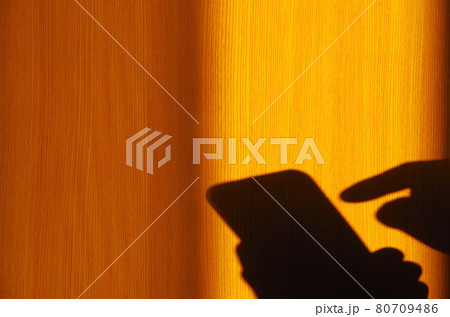 部屋の窓から西日が差してスマホを持つ手と操作する手の影が奥の襖に映る情景 80709486