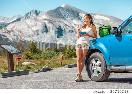 Road trip woman taking a break from driving eating food lunch by her car on summer camping vacation travel. Happy outdoor adventure lifestyle Road trip woman taking a break from driving eating food lunch by her car on summer camping vacation travel. Happy outdoor adventure lifestyle 80710218