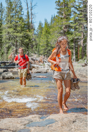 Hikers group walking barefoot in water holding hiking boots crossing river in forest nature, Yosemite. Couple backpackers people on trail hike to cross with backpack and wet feet Hikers group walking barefoot in water holding hiking boots crossing river in forest nature, Yosemite. Couple backpackers people on trail hike to cross with backpack and wet feet 80710220