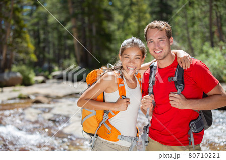 Happy hikers couple hiking in summer forest camping with backpacks. Two friends, Asian woman, Caucasian man smiling portrait, interracial group Happy hikers couple hiking in summer forest camping with backpacks. Two friends, Asian woman, Caucasian man smiling portrait, interracial group 80710221