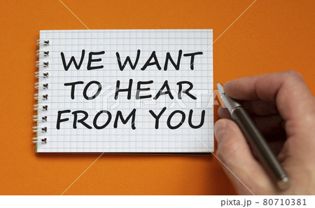 Support symbol. White note with words 'we want to here from you'. Businessman hand with pen. Beautiful orange background, copy space. Business and support concept. Support symbol. White note with words 'we want to here from you'. Businessman hand with pen. Beautiful orange background, copy space. Business and support concept. 80710381